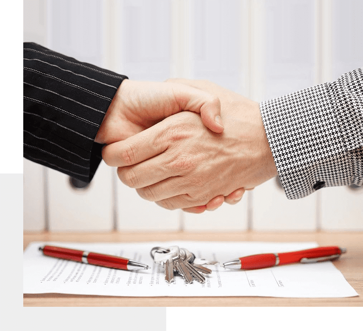 Two people shaking hands over a table with keys.