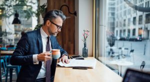 A man in a suit and tie sitting at a table with a cup of coffee.