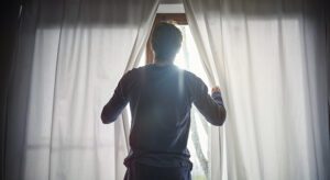 A man standing in front of a window opening curtains.