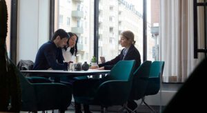 A group of people sitting at a table in front of windows.