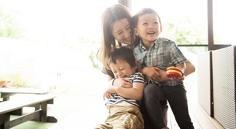 A woman holding two children and smiling.