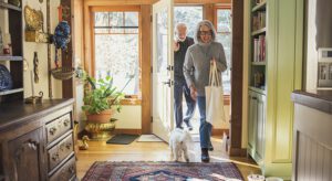 A woman and man walking their dog through the door way.