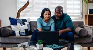 A man and woman sitting on the couch looking at a laptop.