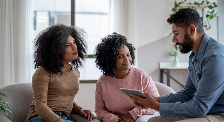 Three people sitting on a couch looking at something.