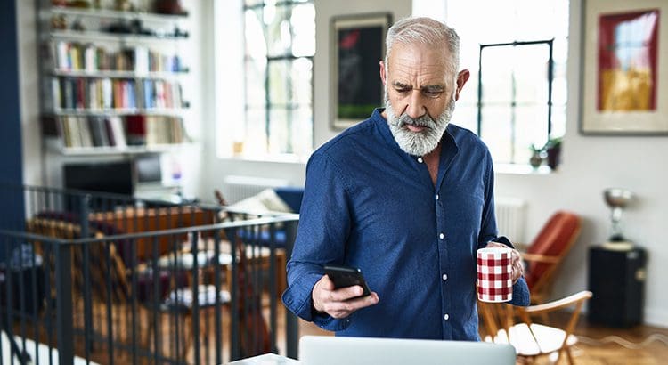 A man standing in front of a laptop holding a cell phone.