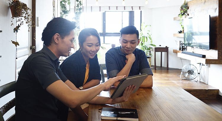Three people sitting at a table looking at an ipad.