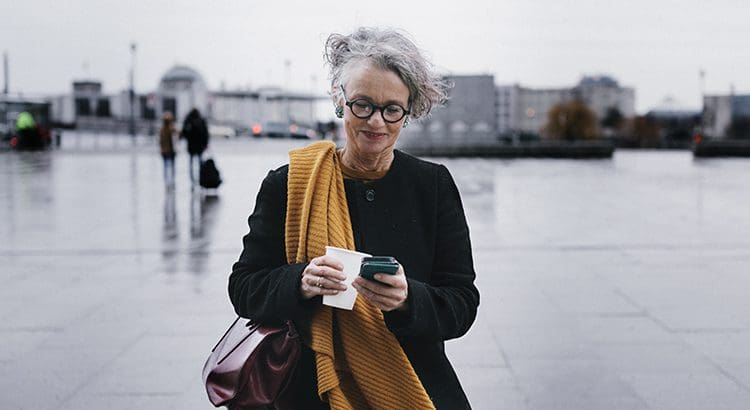 A woman standing on the sidewalk looking at her phone.