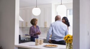 Three people standing in a kitchen talking to each other.
