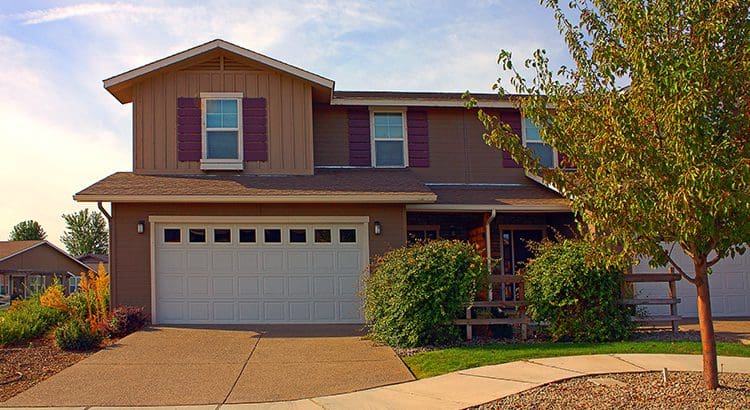 A brown house with red shutters and white garage door.