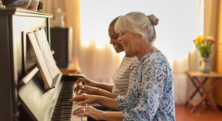 Two women sitting at a piano together smiling.