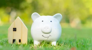 A white piggy bank sitting in the grass next to a house.