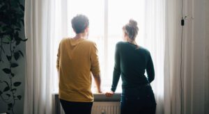 Two people standing in front of a window looking out.