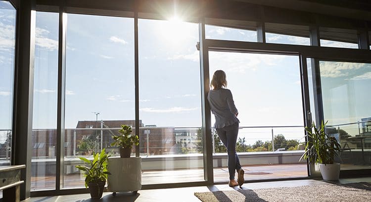A woman standing in front of a window looking out.