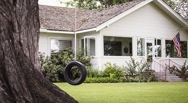 A tire swing hanging from the side of a house.