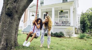 Two girls on a swing in front of a house.