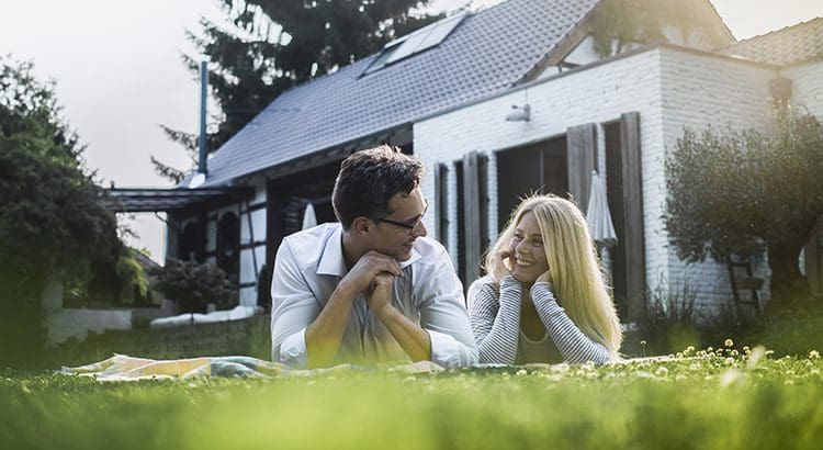 A man and woman sitting on the grass in front of a house.