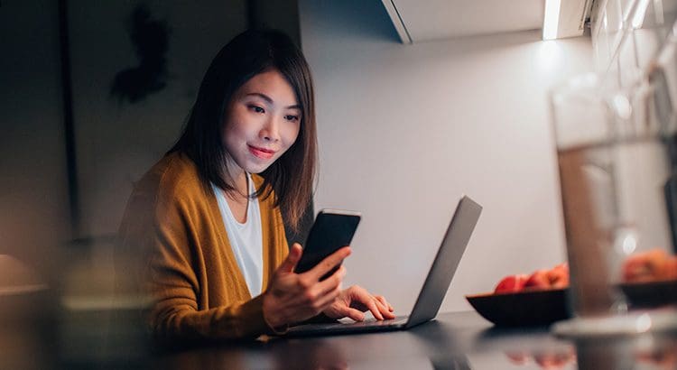 A woman sitting at a table with her phone and laptop.