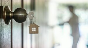 A key with a house shaped keychain hanging from the handle of a door knob.
