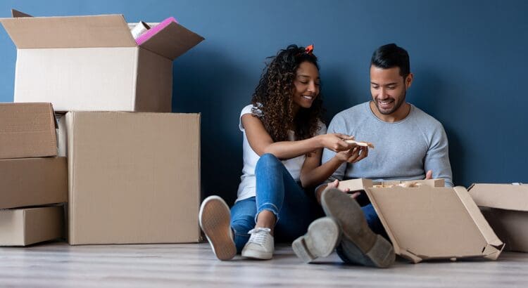 A man and woman sitting on the floor next to boxes.