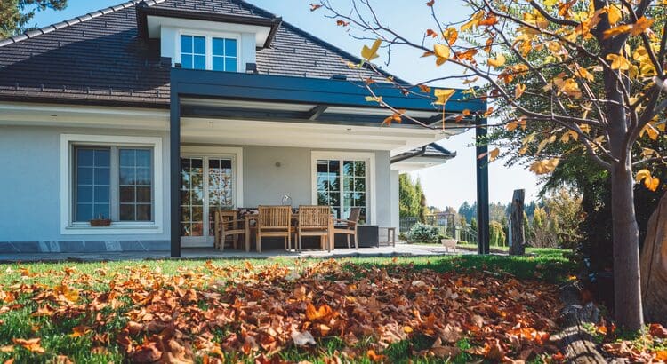 A house with leaves on the ground and chairs in front of it.