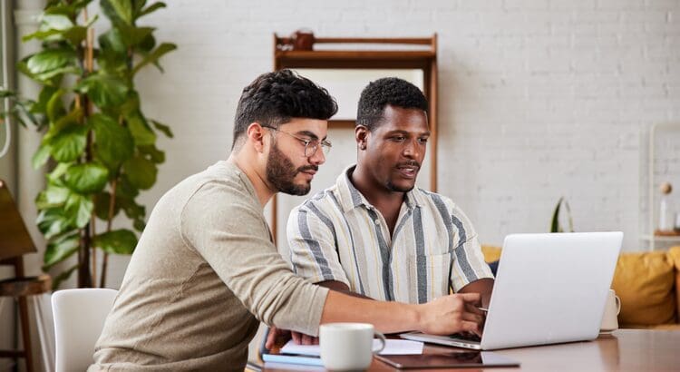 Two men sitting at a table looking at a laptop.