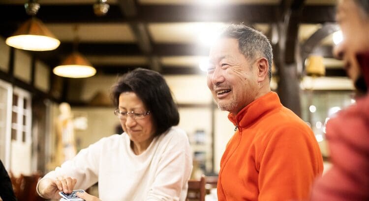 Smiling man in orange shirt playing cards.
