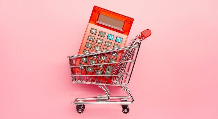 Calculator in shopping cart on pink background.
