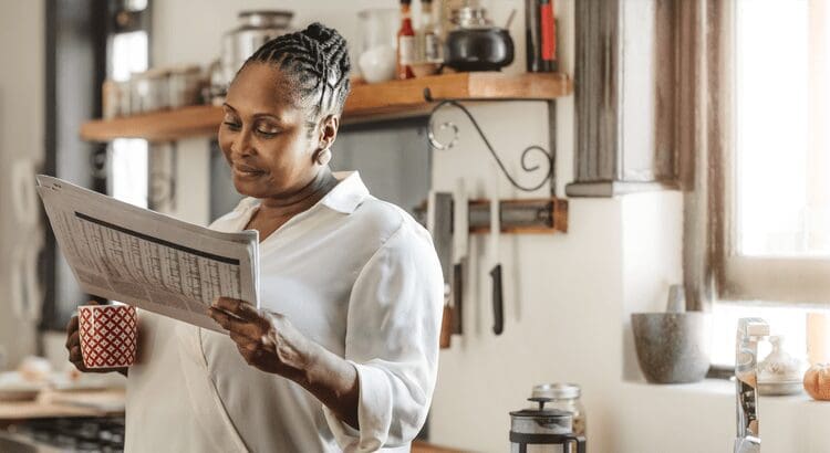 Woman reading newspaper in cozy kitchen setting.