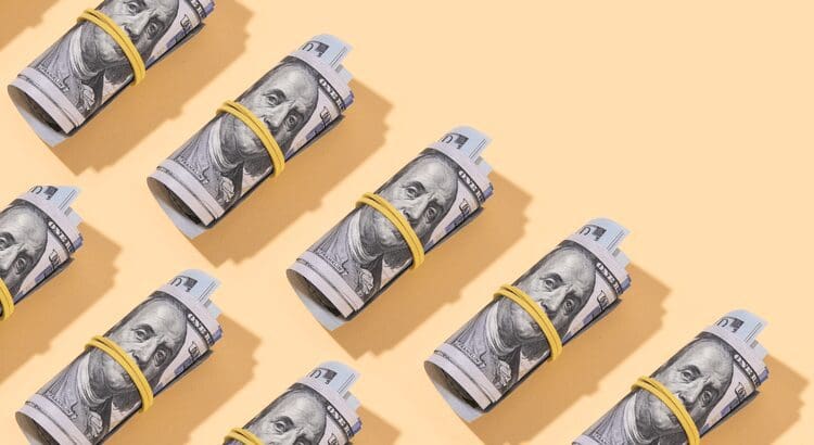 Rolled dollar bills on peach background.
