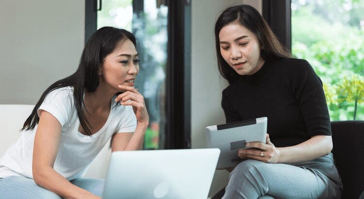 Two women working on laptop and tablet.
