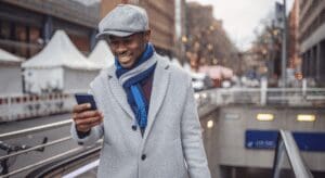 Man in coat smiling at smartphone outdoors.
