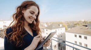 Smiling woman using tablet on balcony.