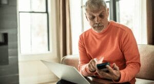 Senior man using smartphone and laptop at home