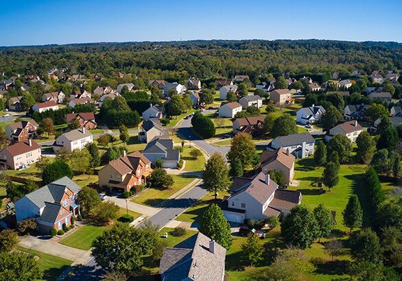 Shot using a drone during the golden hour shows an upscale suburbs with gold course, lake, houses and roof tops