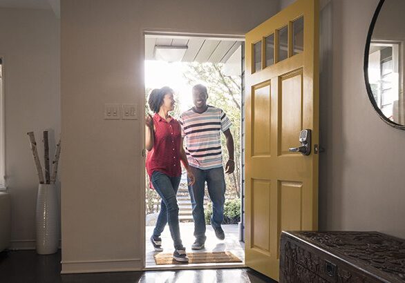 Young man and woman stepping into the house, they are happy and smiling as they come through the open yellow door