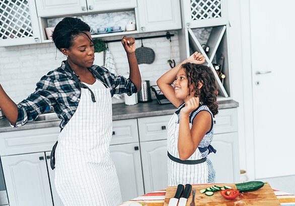 Mixed race mother and daughter dancing while cooking together in the kitchen