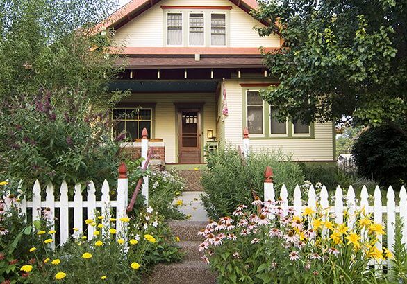 A house with flowers growing around it and a white picket fence.