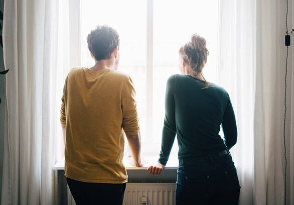 Rear view of couple looking through window while standing at home