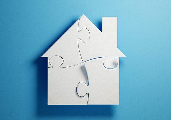White jigsaw puzzle pieces are forming a house shape on blue background. Horizontal composition with copy space. Clipping path is included.