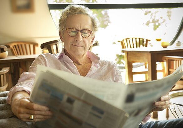 Smiling senior man in lounge room reading newspaper