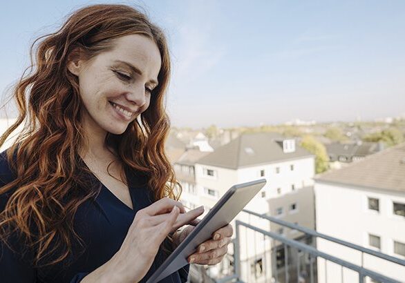 Smiling redheaded woman using tablet on rooftop terrace