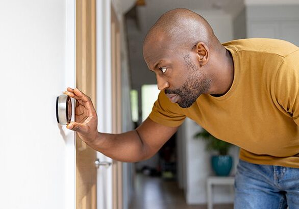 African American man adjusting the temperature on the thermostat of his house - home automation concepts