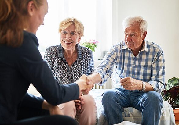 Financial advisor shaking hands with senior man in living room. Retired couple in meeting with a female financial advisor at home.