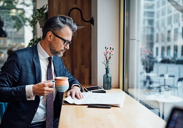 Mature businessman reading paper while having coffee at a coffee shop. Man in business suit drinking coffee and reading newspaper at cafe.