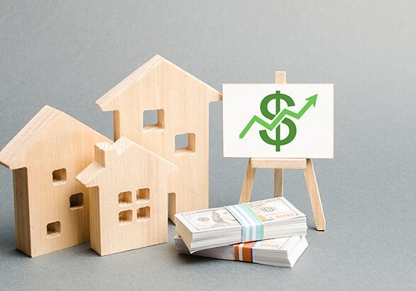 Wooden figures of houses and a poster with money. The concept of real estate value growth. Increase liquidity and attractiveness of assets. Raising the rent or cost of buying a home.