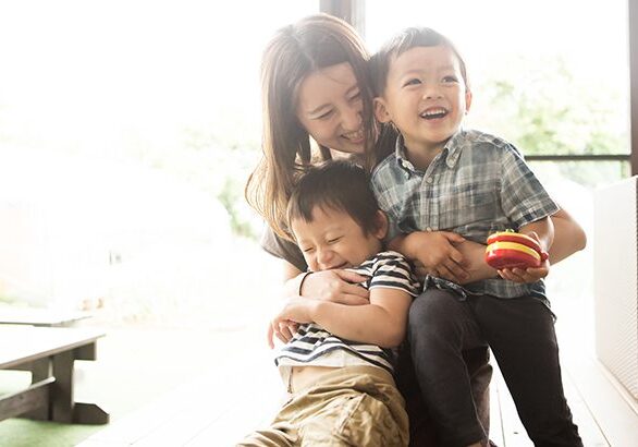 A woman holding two children and smiling.