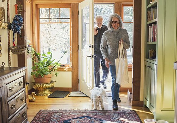 A woman and man walking their dog through the door way.