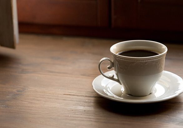 One glass of black tea, chicory or coffee on a light wood table, on a window sill near a window, in a cafe, cafeteria or at home. The concept of loneliness, breakfast. Coffee break. A copy of the space.
